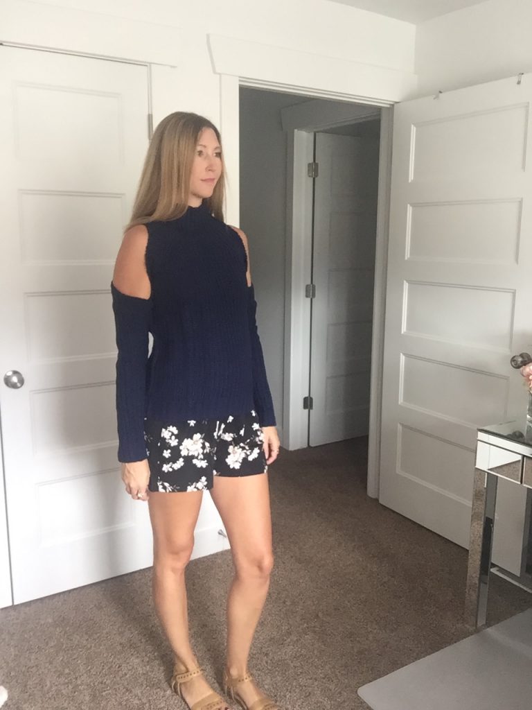 woman in Navy open shoulder sweater and floral black shorts